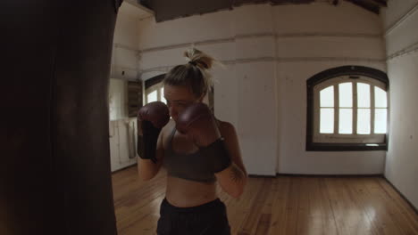 Tracking-shot-of-woman-in-boxing-gloves-punching-heavy-bag